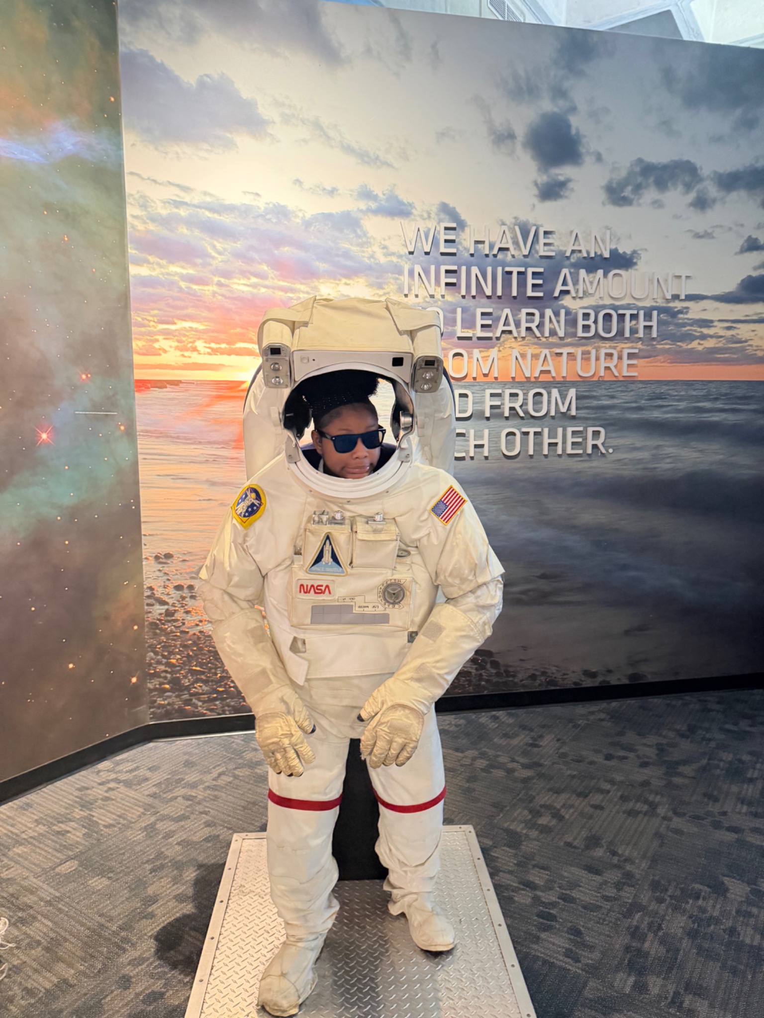A student in sunglasses trying an astronaut suit exhibit